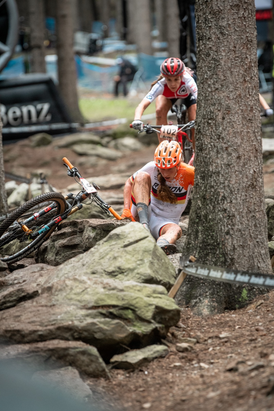 Elisabeth Brandau nach einem Sturz beim Mountainbike-Rennen, im Hintergrund fährt eine Konkurrentin vorbei